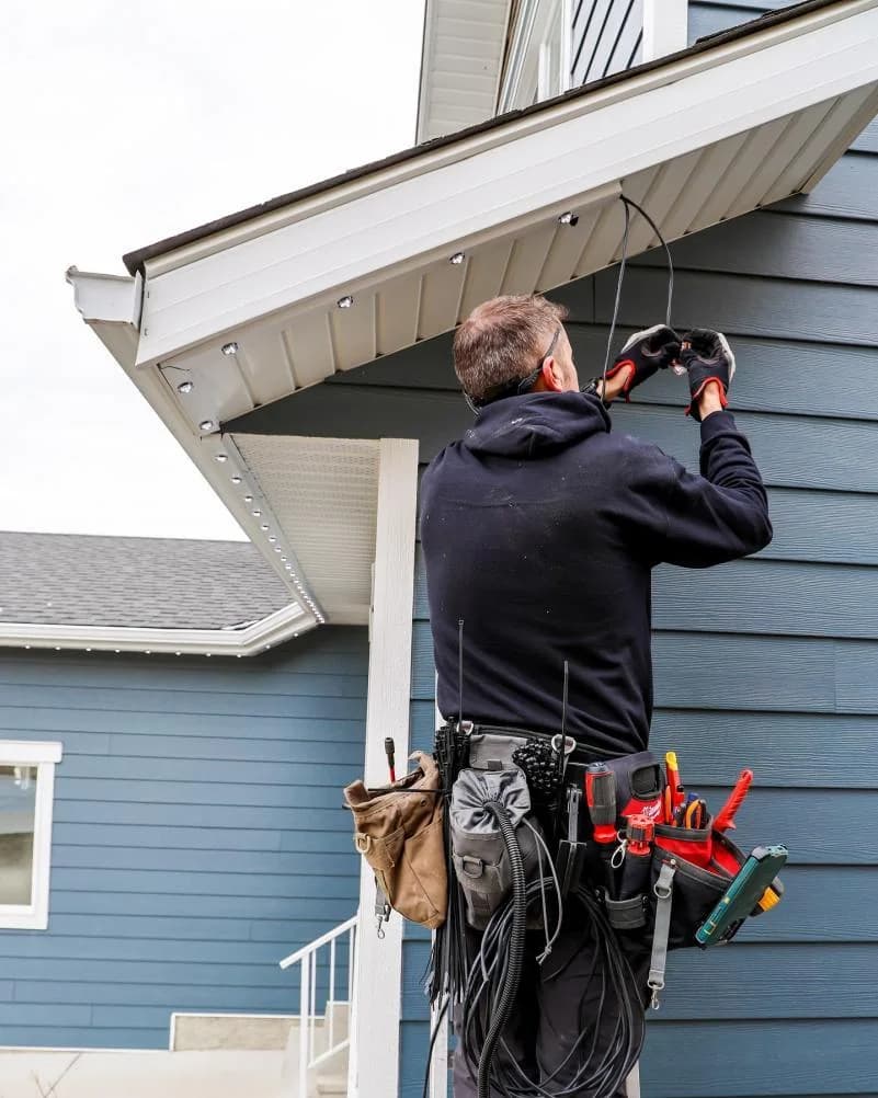 Professional installer routing permanent RGBW pixel light wiring at a residential roofline