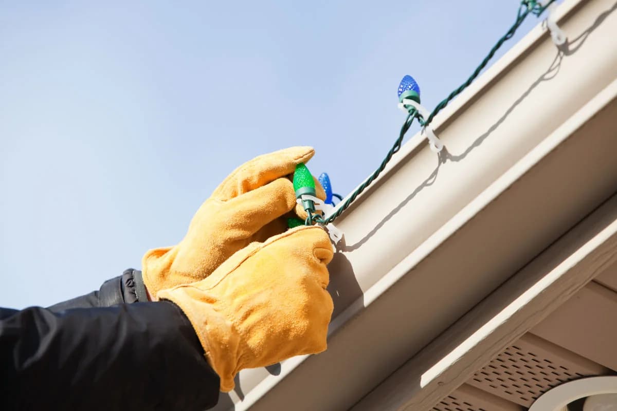 Professional installer attaching C9 Christmas lights to a residential gutter