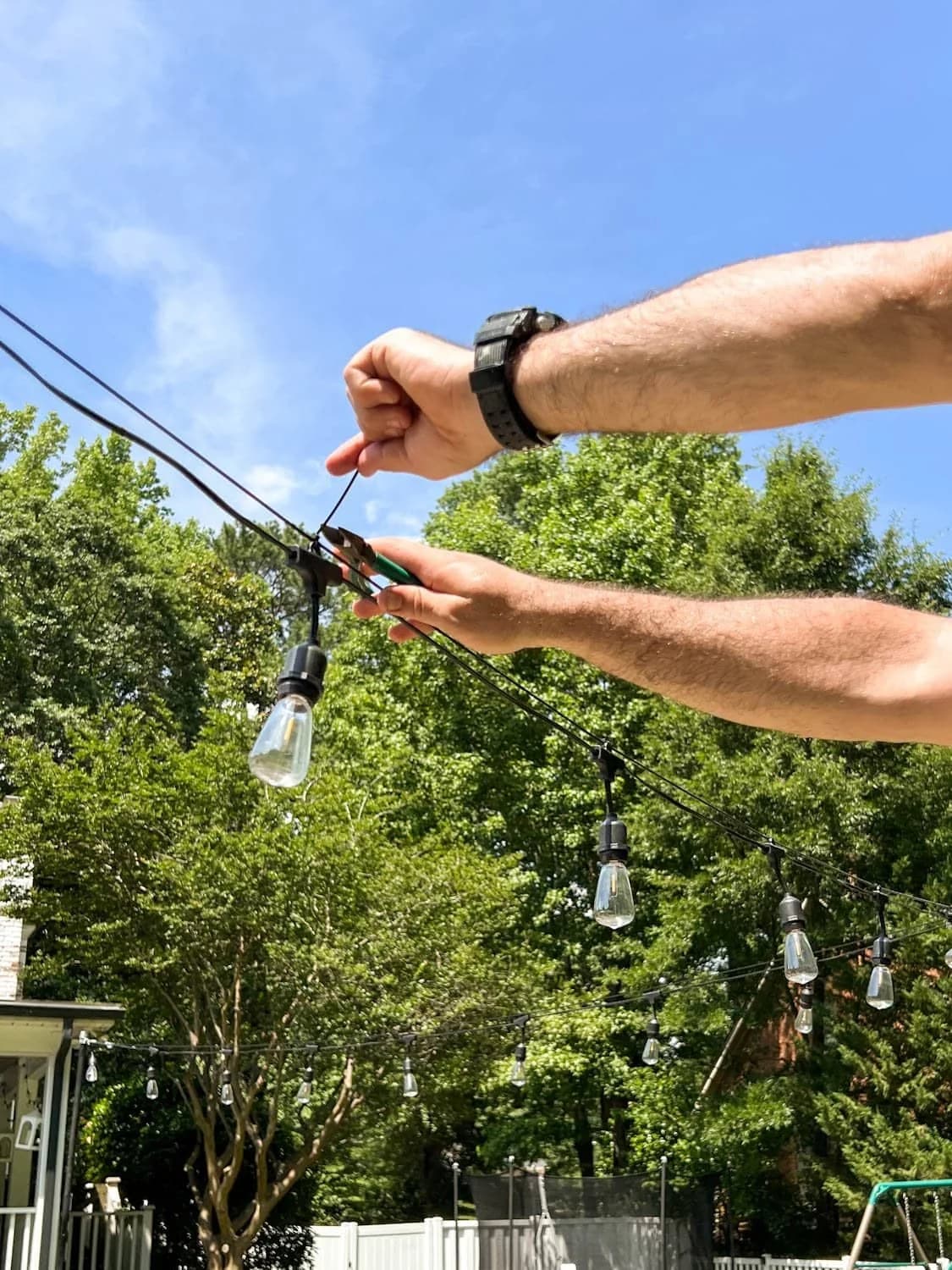 Installer fastening commercial string lights to an overhead guide wire